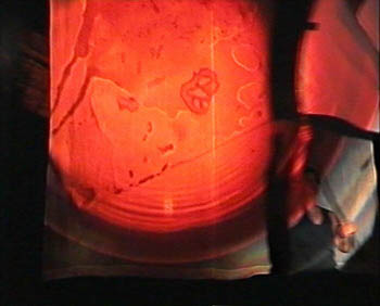 A flag is being waved in front of a projection screen. A large, glowing red circle is projected onto them.
