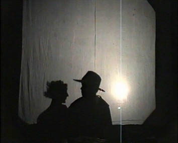 Profile shadows of Agnes and Matilda in a secret meeting are projected on to a white screen.